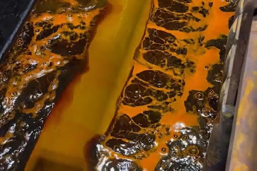 Industrial chrome plated rolls submerged in an orange chemical plating bath solution.